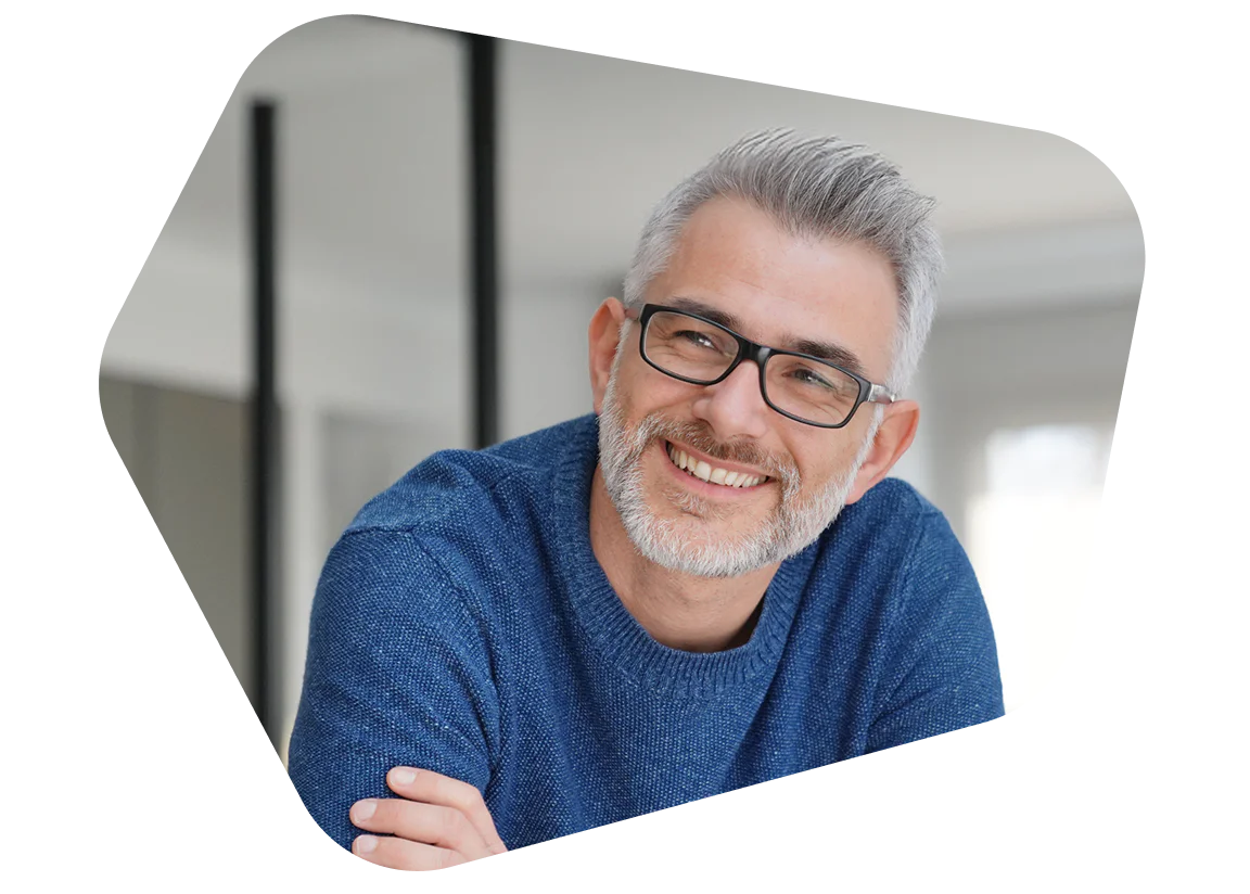 Smiling man with glasses in blue sweater indoors Man with grey hair and glasses wearing a blue sweater smiling indoors