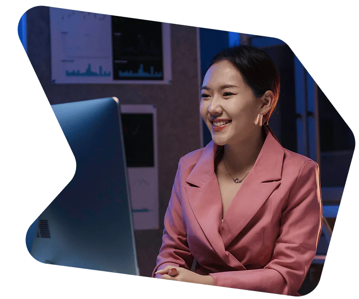 Businesswoman in pink blazer working late at office Woman in a pink blazer smiling and working at a computer in a dimly lit office