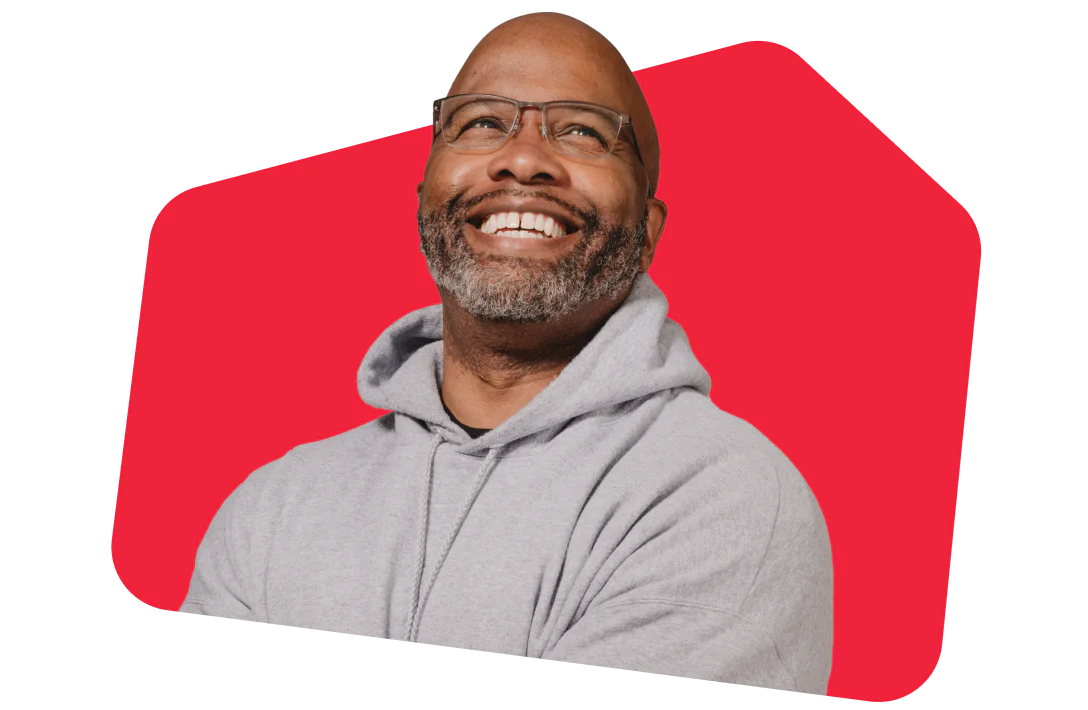 Smiling man in glasses and hoodie against red background Man with glasses and gray hoodie smiling in front of a red background