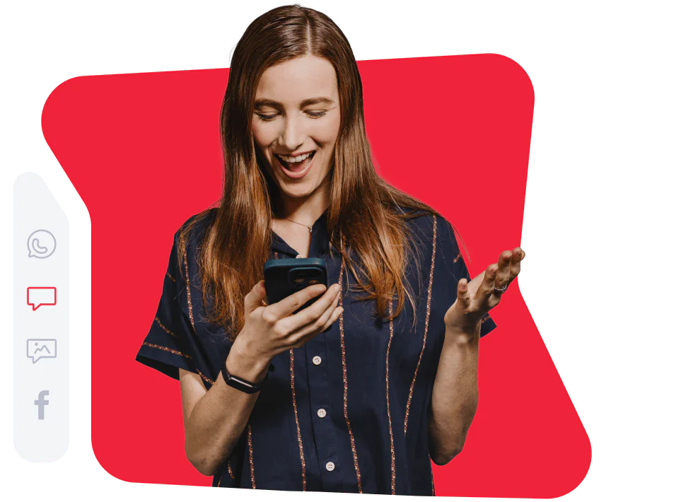 Woman smiling and reacting to a message on phone Woman in a navy shirt smiling while looking at her phone with a red background.